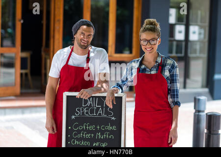 Portrait of smiling waitress and waiter standing with menu sign board outside cafÃƒÂ© Stock Photo