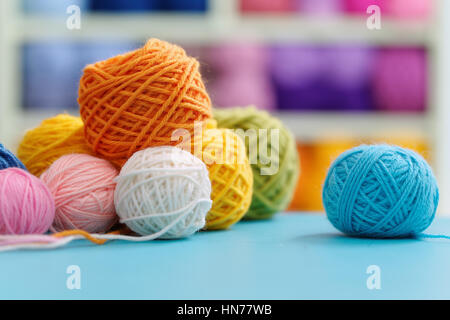 Knitting yarn on blue table against blurred background. Close up of multi colored woolen balls. Stock Photo