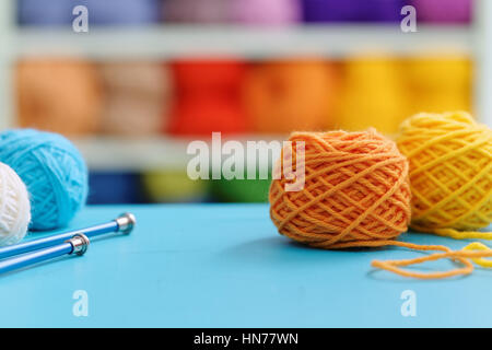 Knitting yarn and needles on blue table against blurred background. Close up of multi colored woolen balls. Stock Photo