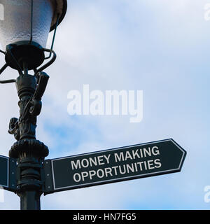 Street lighting pole with conceptual message MONEY MAKING OPPORTUNITIES on directional arrow over blue cloudy background. Stock Photo