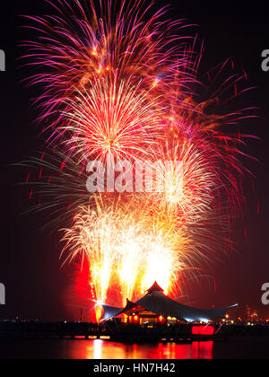 Spectacular fireworks explosion in the sky of night and silhouette of cafe on a pier at Lagoon Beach, Ancol, North Jakarta. Shot with long exposure te Stock Photo