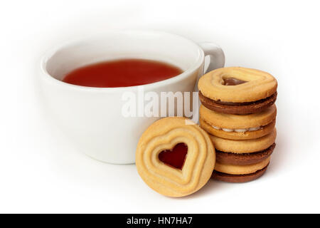 A cup of tea with a butter cookie with heart-shaped chocolate filling, with more cookies in the background, on white background Stock Photo
