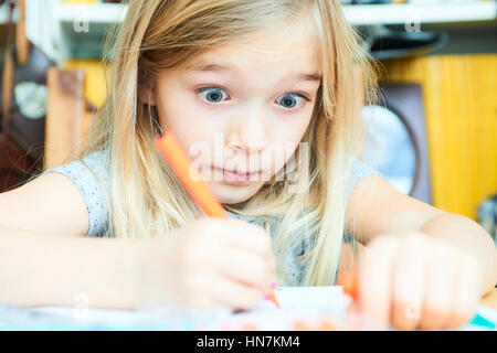 Funny little child girl is drawing and painting with colorful felt-tip pens. Preschooler girl creating at home sitting at table. Stock Photo