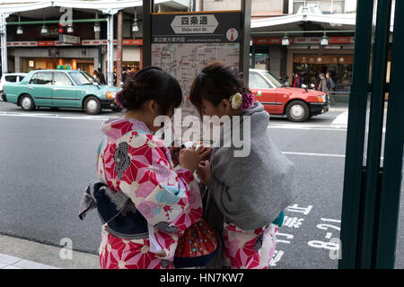 Two geishas in Kyoto, Japan, Asia looking for directions on map, using mobile phone or smartphone. Young Asian women in traditional Japanese dress Stock Photo