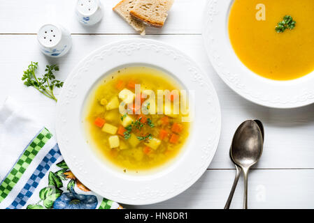 Two plates of vegetable soup and cream with bread fresh parsley, spoons, salt and pepper shakers on white wooden table Stock Photo