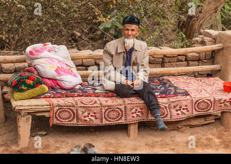 Old Uighur man sitting on bench, Toyuq village, Xinjiang Autonomous Region, China. Stock Photo