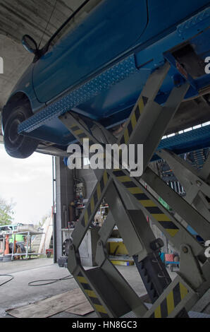 A car raised on a lift for repair and under it a detached Transmission ...