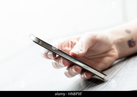 Young woman with tattoos on her wrist holding a modern smartphone in her hand as she texts a message, close up side view Stock Photo