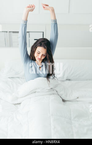 Beautiful woman waking up in her bed in the bedroom, she is stretching and smiling Stock Photo