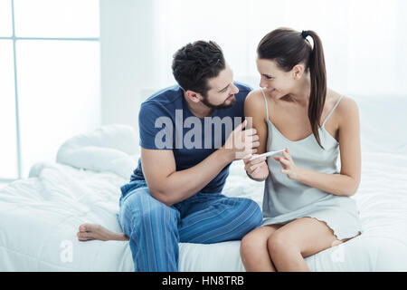 Young loving couple taking a pregnancy test, they are sitting in bed together and smiling Stock Photo