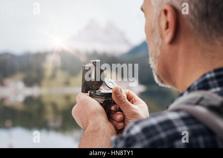 Hiker trekking on the mountains and exploring nature, he is using a hiking compass and searching directions Stock Photo