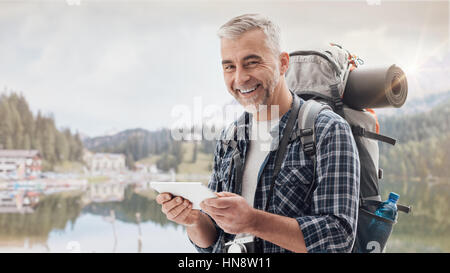 Hiker trekking on the mountains and connecting with a digital touch screen tablet using an outdoor wireless access point Stock Photo