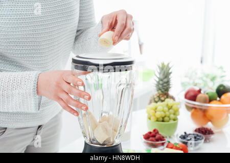 Woman putting a banana in a blender and preparing a delicious healthy smoothie in her kitchen Stock Photo
