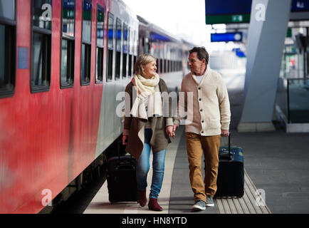 Senior couple on train station pulling trolley luggage. Stock Photo