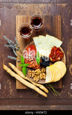 Snacks on a clay plate with wine Marsala . on wooden background. rural style. prosciutto, cheese, prunes, apples, walnuts