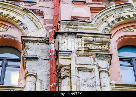 Details of an old building with deteriorated and dilapidated front face. Dark windows and orange painted heavily used rain pipe or water spout. Stock Photo