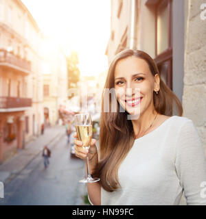 Young beautiful happy woman standing with glass of champagne on balcony outdoor Stock Photo