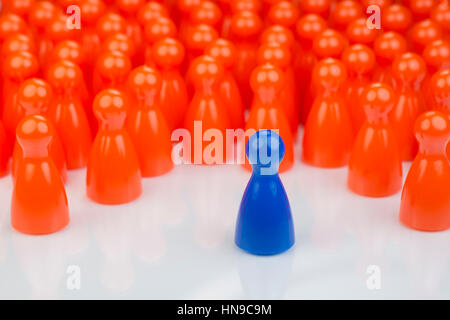 Conceptual orange game pawns and a blue play pawn as abstract display of inequality in color and number of Stock Photo