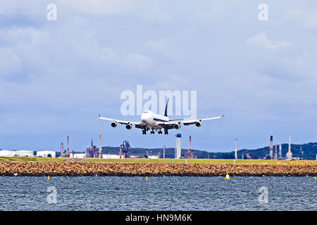 Huge jet airplane landing on Airport runway in Sydney against cargo terminal and blue sky. Stock Photo