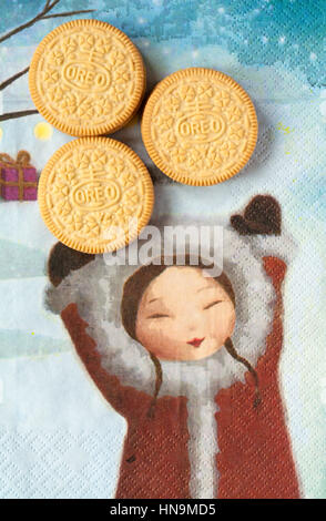 Three Golden Oreo biscuits on serviette with girl holding hands up, sandwich biscuits with a vanilla flavour filling Stock Photo