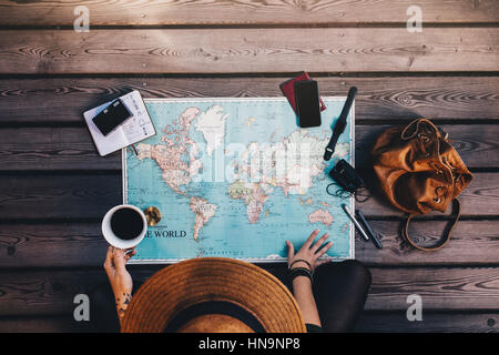 Young woman planning vacation using a world map, compass and other travel accessories. Tourist looking at the world map holding a cup of coffee. Stock Photo