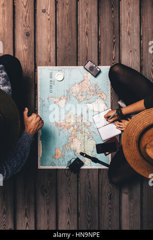 Top view of man and woman planning vacation using a world map. Woman noting plan in a diary. Stock Photo