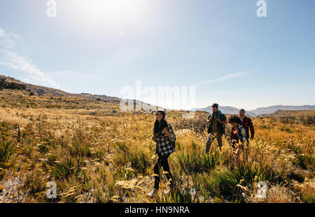 Group of friends are hiking in mountain on a sunny day. Four young people walking through countryside. Stock Photo