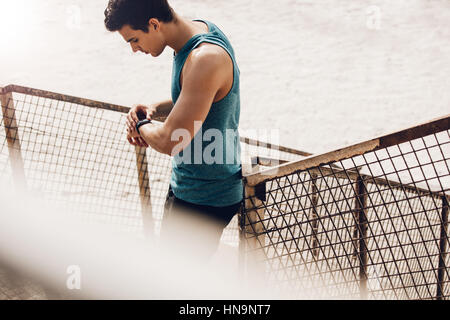 Young man checking progress on smart watch during workout. Muscular young male runner checking his performance in morning. Stock Photo