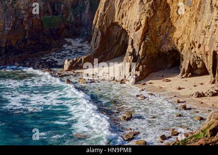A sunny winters midday, looking down from the South West Coast Path at the waves breaking in a small cove, blue sea, golden yellow sand and cliff face Stock Photo