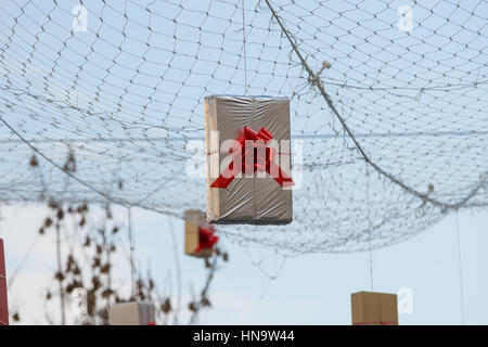 Gift boxes that hang suspended on wires and networks. Street decorations before Christmas, New Year and Valentine's Day. Stock Photo