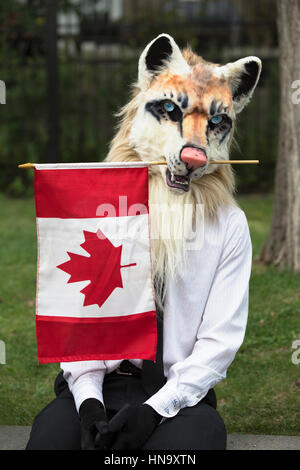 Man wearing animal mask holding Canadian flag during Canada Day celebration Stock Photo