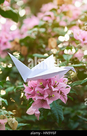 white paper crane in garden with pink flowers Stock Photo