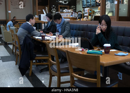 Young Korean student studying with phone and ipad tablet, Asian people working in a cafeteria, busy businessmen with papers. Seoul, South Korea, Asia Stock Photo