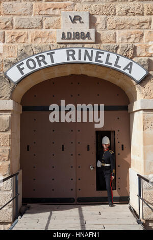 A site guide in period British military uniform stepping out of the main door of Fort Rinella in Malta. Stock Photo