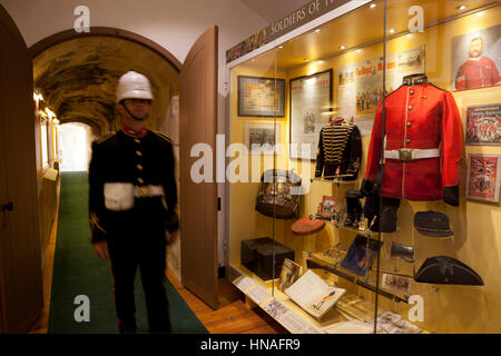A site guide in historial British military uniform walks past displays of nineteenth century British military artifacts and colonial paraphernalia exh Stock Photo