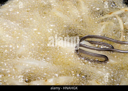 french fries frying in hot bubbling oil, tongs turning stirring during cooking Stock Photo