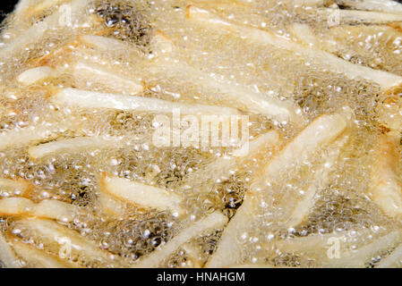 Medium sized Russet potatoes peeled, sliced and frying in hot oil creating home made french fries. An inexpensive alternative to fast food restaurants Stock Photo