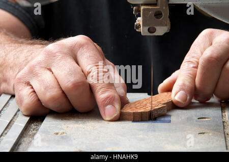 Male hands holding a small piece of wood precision cutting on a table top jig saw. Saw dust everywhere. Stock Photo