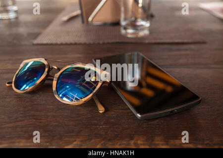 Smart phone and hipster sunglasses on wood bar table, blank screen and selected focus Stock Photo