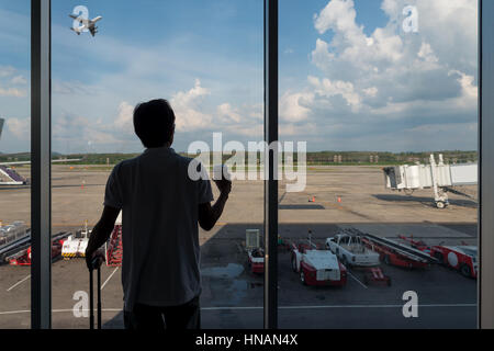 Back side of traveler boy in termainal at airport looking at the flying plane above airport, travel and vacation lifestyle concept Stock Photo