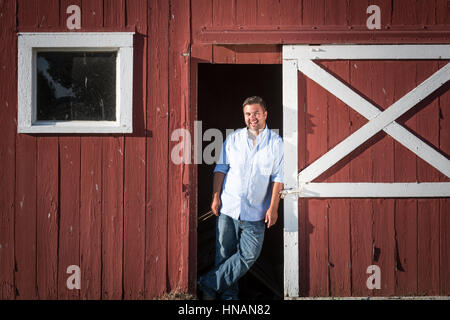 Portrait of a chicken farmer leaning on a red barn door on his farm located on Maryland's Eastern shore. Stock Photo