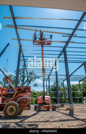 Workers hold beams on a cherry-picker while working on the construction of a new industrial building. Stock Photo