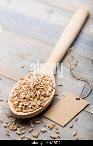 heap of spelt in wooden spoon on table with label for text. Stock Photo