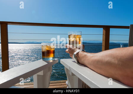 Two drinks on seaside deck with mans arm holding one up. Stock Photo