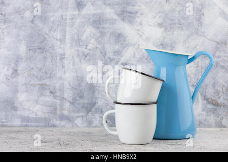 Two white enamel mugs and blue pitcher on light background Stock Photo