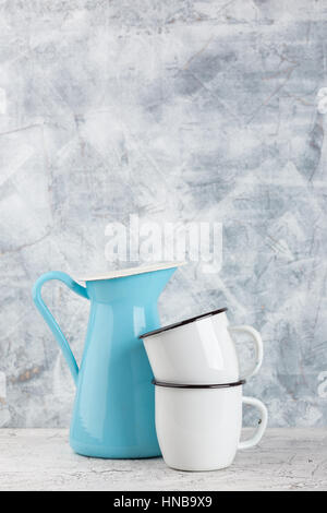 Two white enamel mugs and blue pitcher on light background Stock Photo