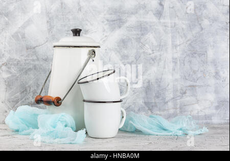 Two white cups and white enameled cans on light background Stock Photo