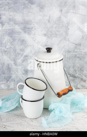 Two white cups and white enameled cans on light background Stock Photo