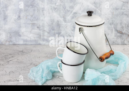 Two white cups and white enameled cans on light background Stock Photo