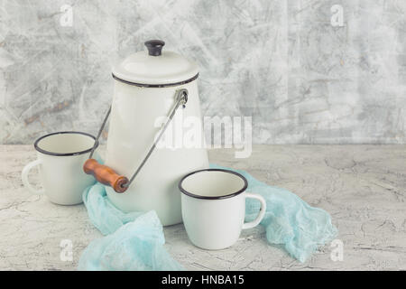 Two white cups and white enameled cans on light background Stock Photo